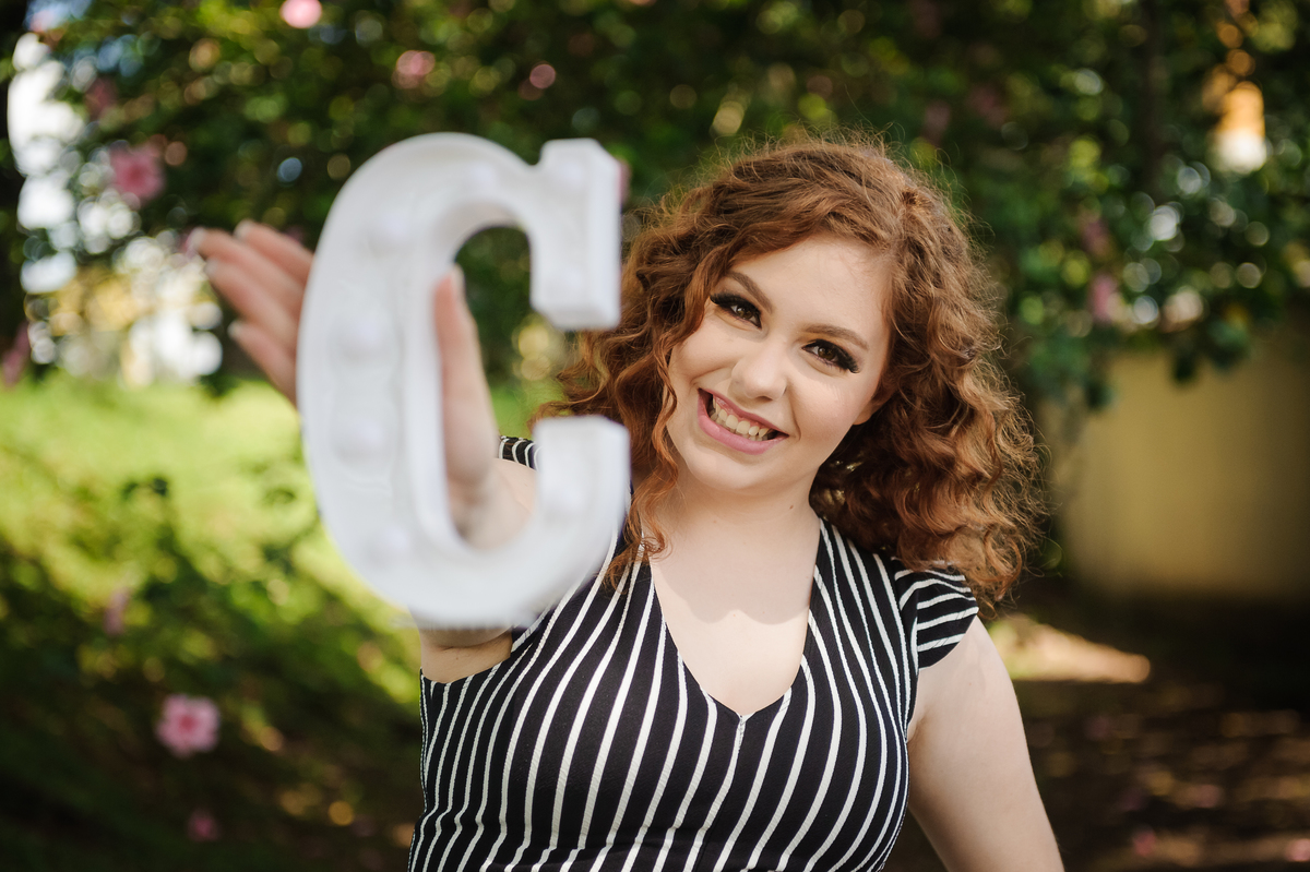 Menina 15 anos segurando placa com a letra do seu nome no book de fotos de aniversário de 15 anos