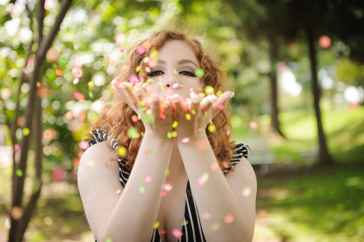 Menina 15 anos brincando com confetes coloridos no seu book de fotos de 15 anos