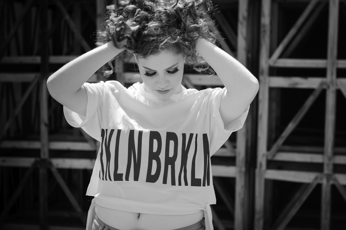 Menina 15 anos posando para foto preto e branco e segurando cabelo na frente de pallets para seu book de fotos de 15 anos