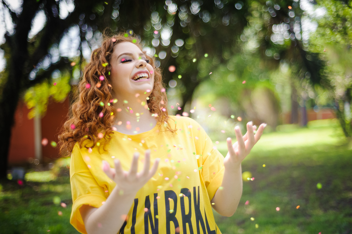 Menina 15 anos brincando com confetes coloridos em pé no seu book de fotos de 15 anos
