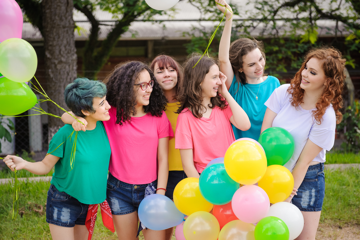 Meninas olhando para aniversariante com balões coloridos e posando para foto de book de 15 anos