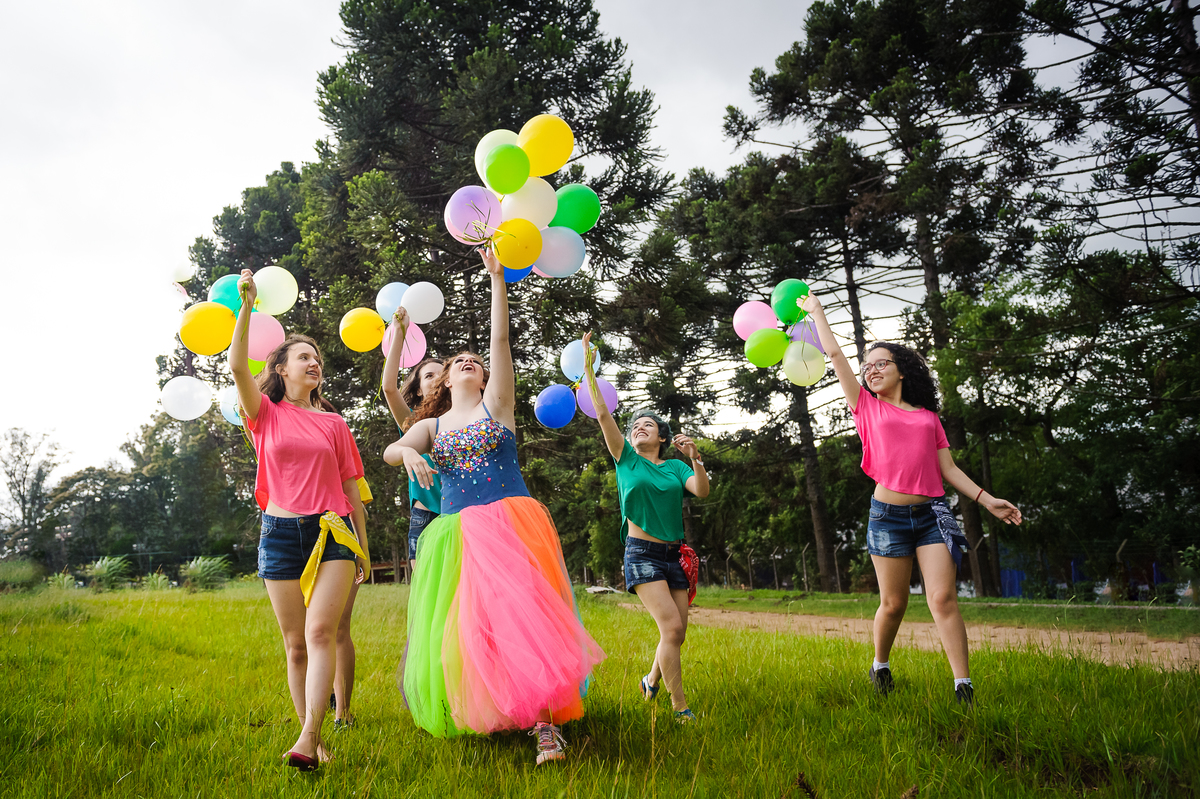 Menina com vestido de tule soltando balões e bexigas coloridos com amigas no seu book de fotos de 15 anos