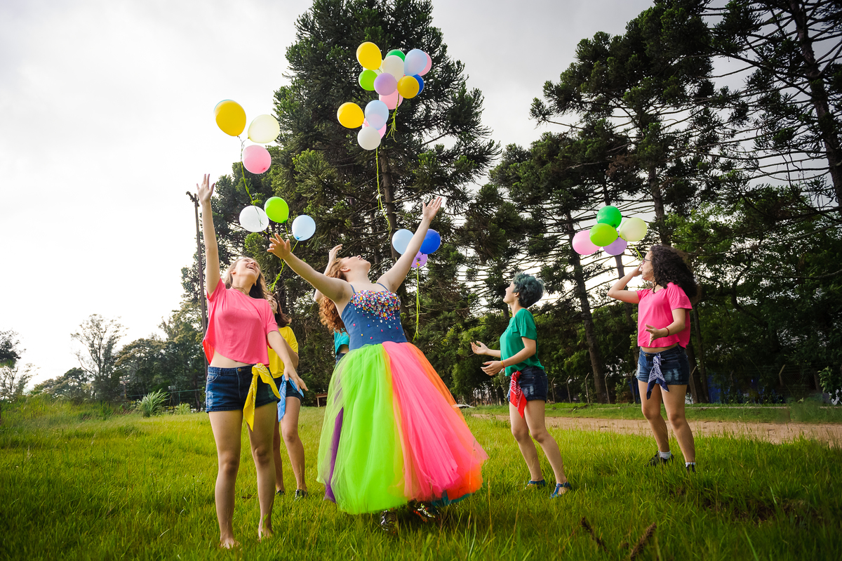 Menina com vestido de tule soltando balões e bexigas coloridos com amigas no seu book de fotos de 15 anos