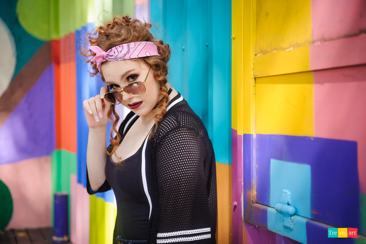 Menina segurando óculos para fotos na parede colorida no seu book de 15 anos