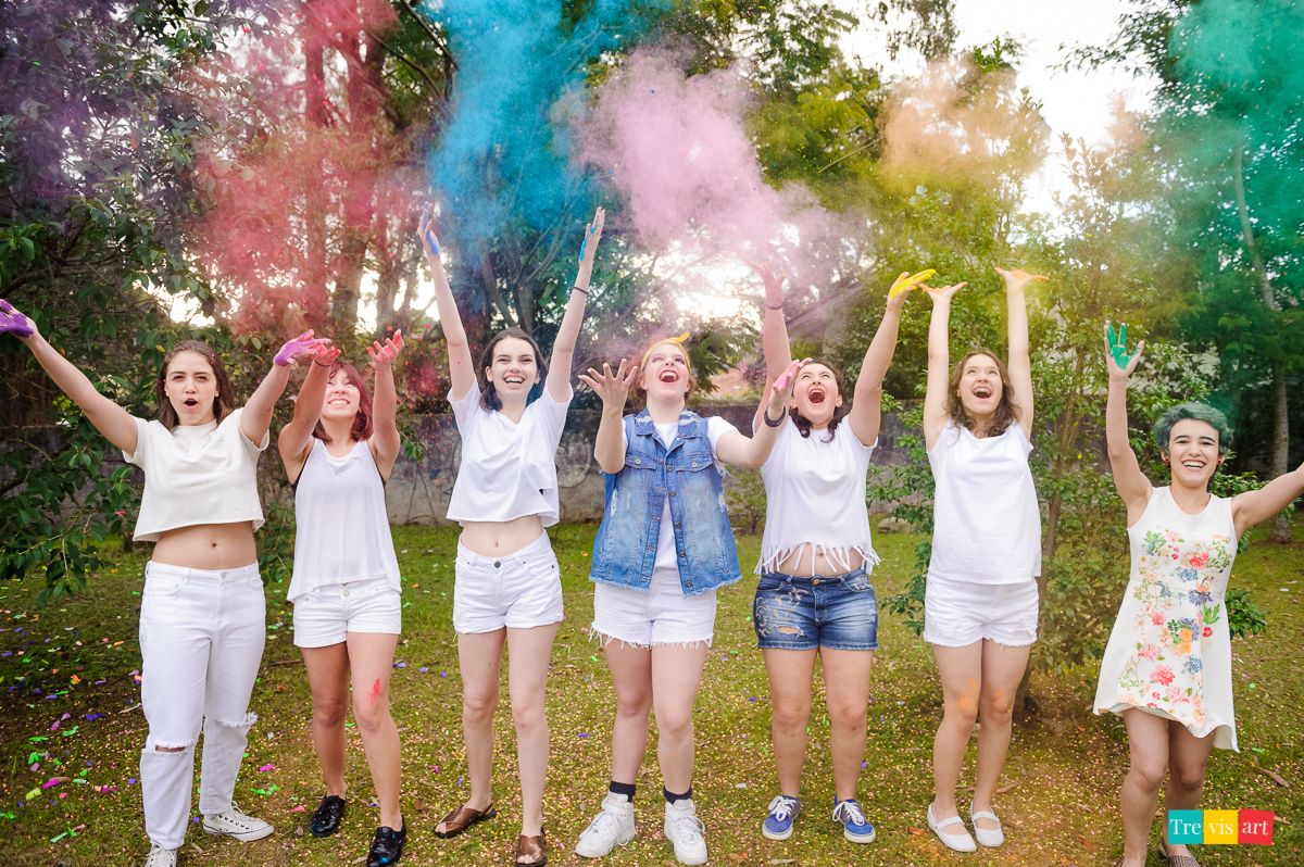 Meninas de branco jogando pó de happy holi coloridos para foto de book de 15 anos da amiga