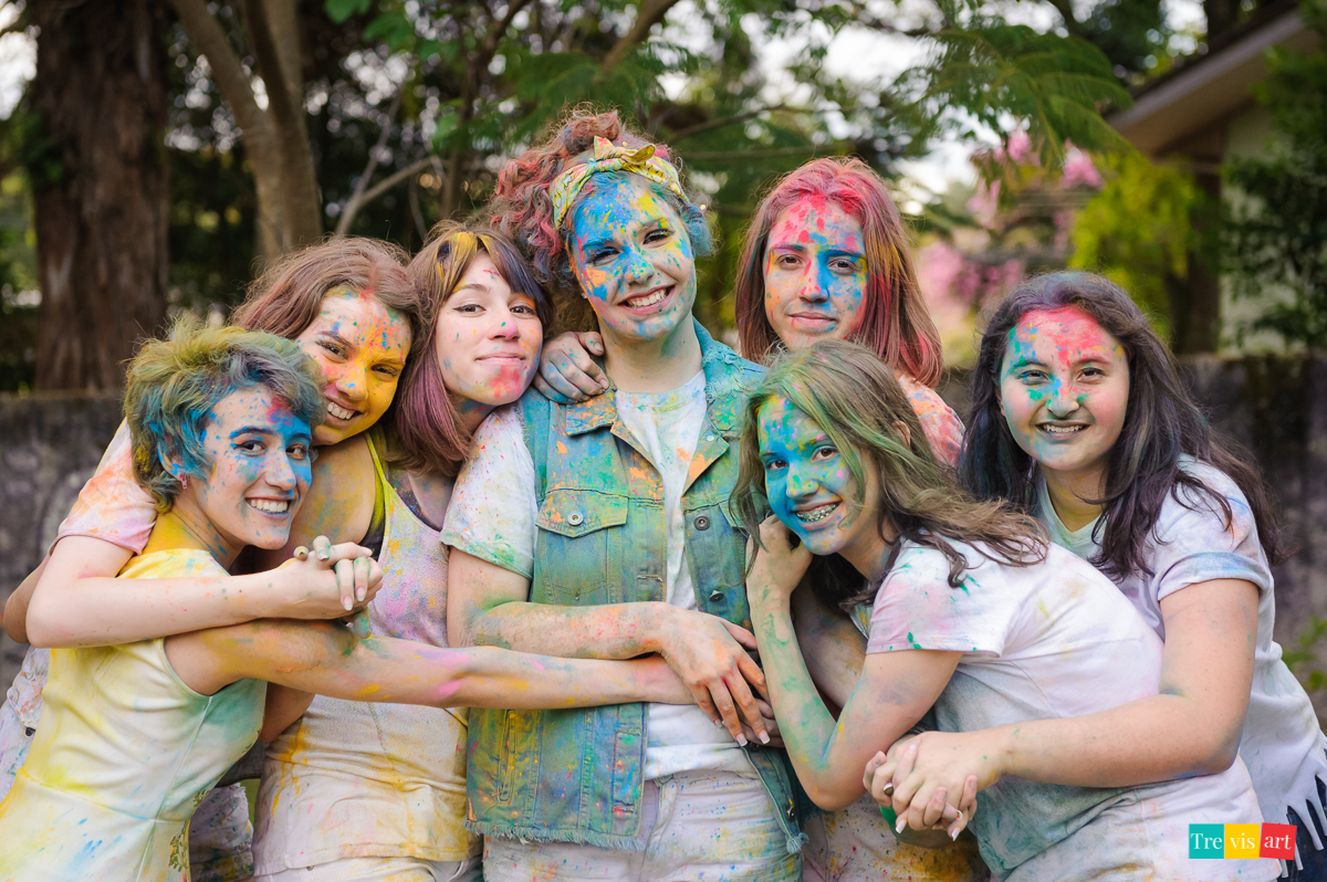 Meninas todas coloridas e abraçadas co as amigas posando para foto com pó de happy holi de todas as cores para fotografia de book de 15 anos da amiga