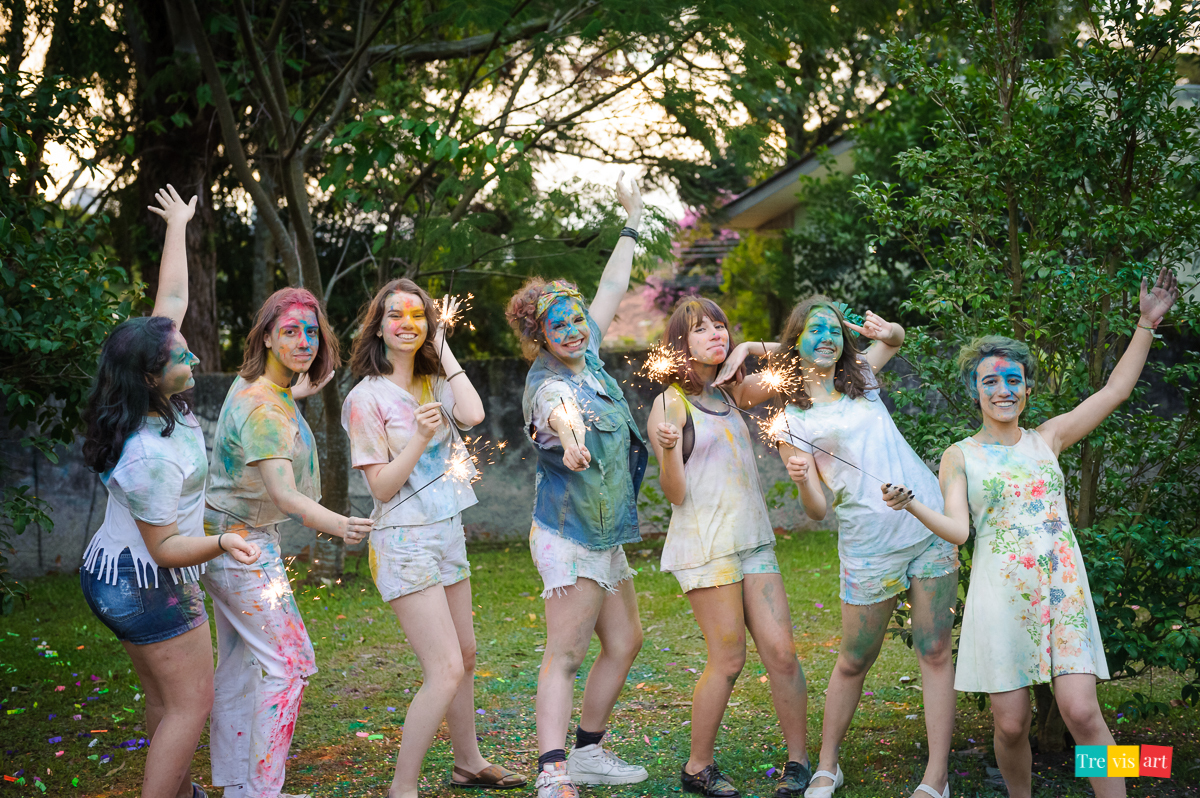 Meninas todas coloridas brincando com luzinhas com as amigas posando para foto com pó de happy holi de todas as cores para fotografia de book de 15 anos da amiga