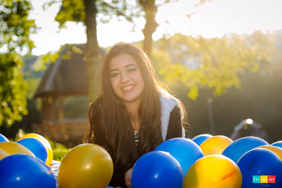 Menina de 15 anos sorrindo em seu book de 15 anos com balões coloridos azul e dourado no memorial ucraniano em curitiba com luz do sol