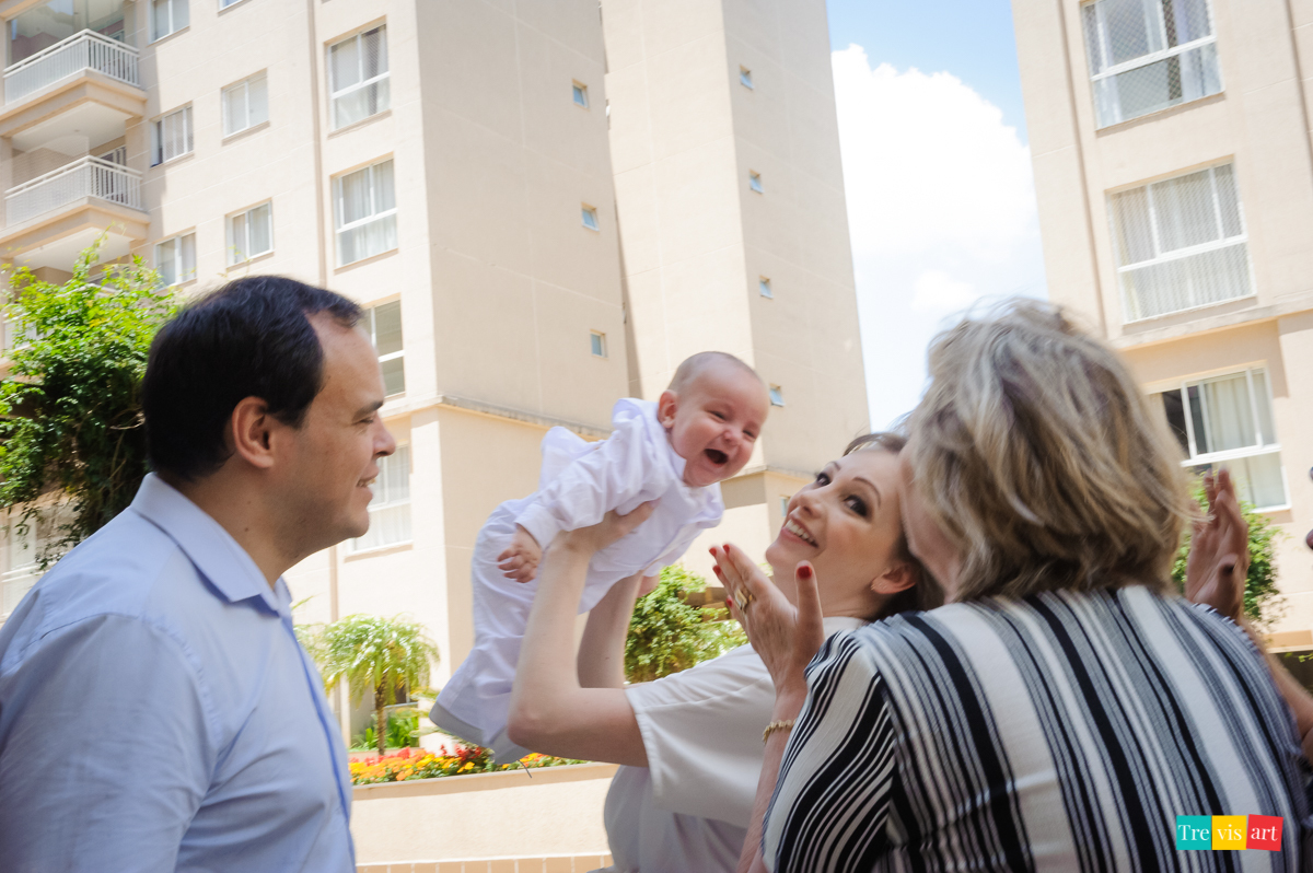 pais e avó brincando com bebê de aviãozinho no almoço de batismo