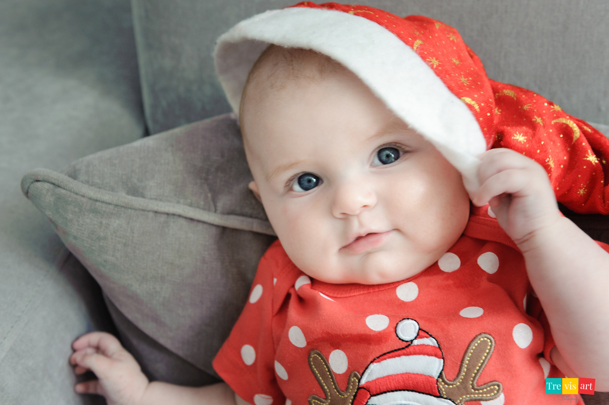 foto do bebê no sofá sorrindo e fazendo charme, com touquinha de natal fotografia de acompanhamento trimestral de bebê