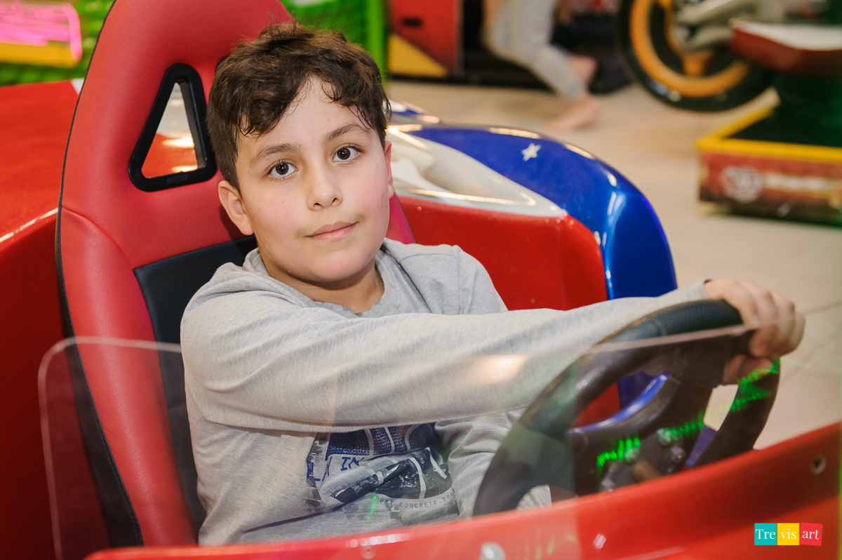 Foto de perto aniversariante brincando no simulador de carro no buffet de festa infantil.