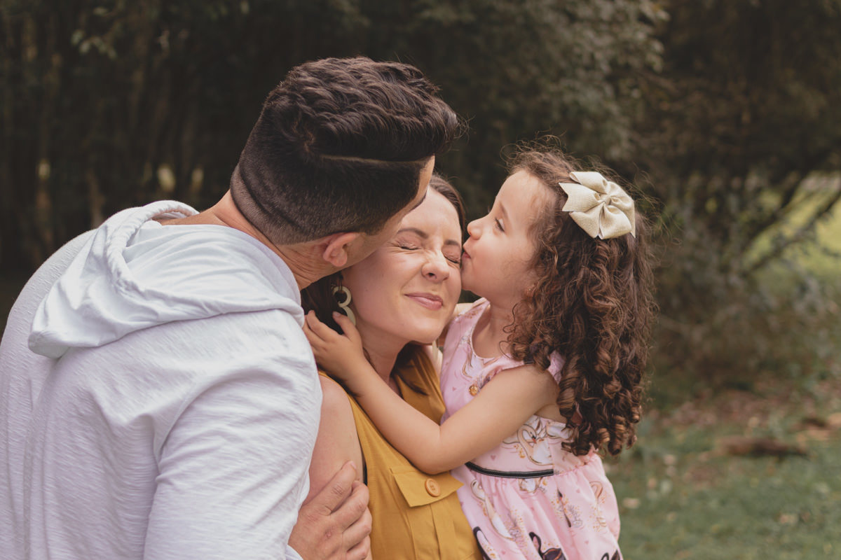 pai e filha beijando a mãe e família brincando no Parque Tingui em Curitiba 