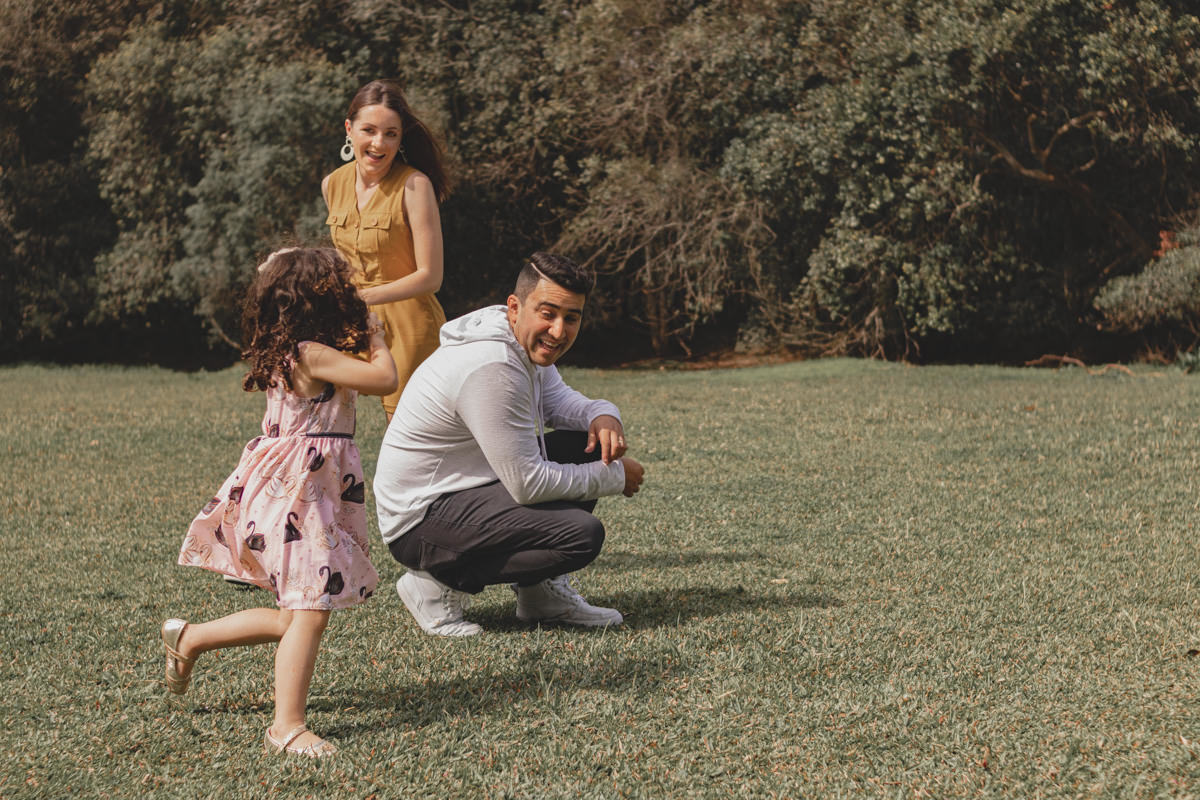 pai, mãe e filha brincando de pique pega no Parque Tingui em Curitiba 