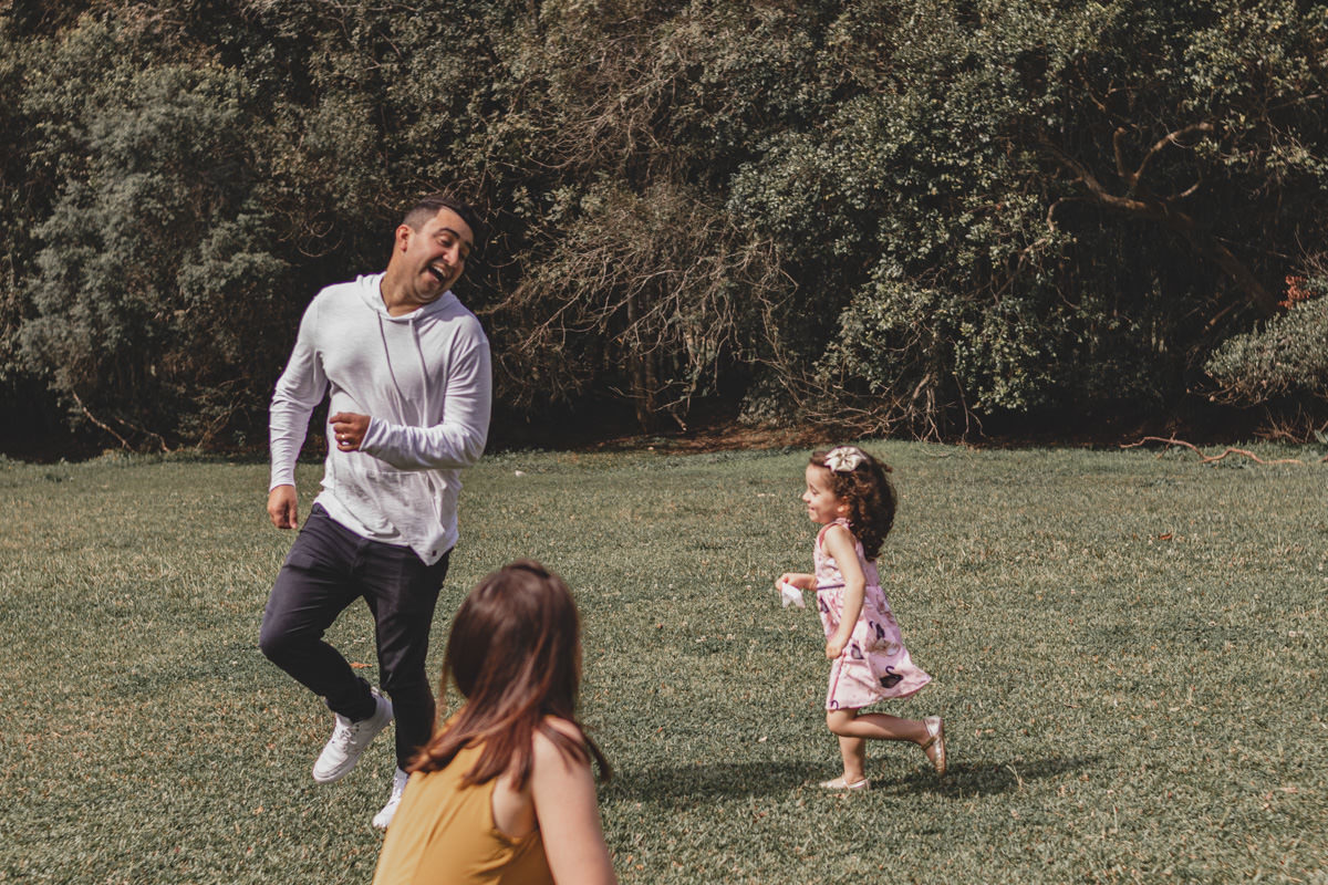 pai, mãe e filha brincando de pique pega no Parque Tingui em Curitiba 
