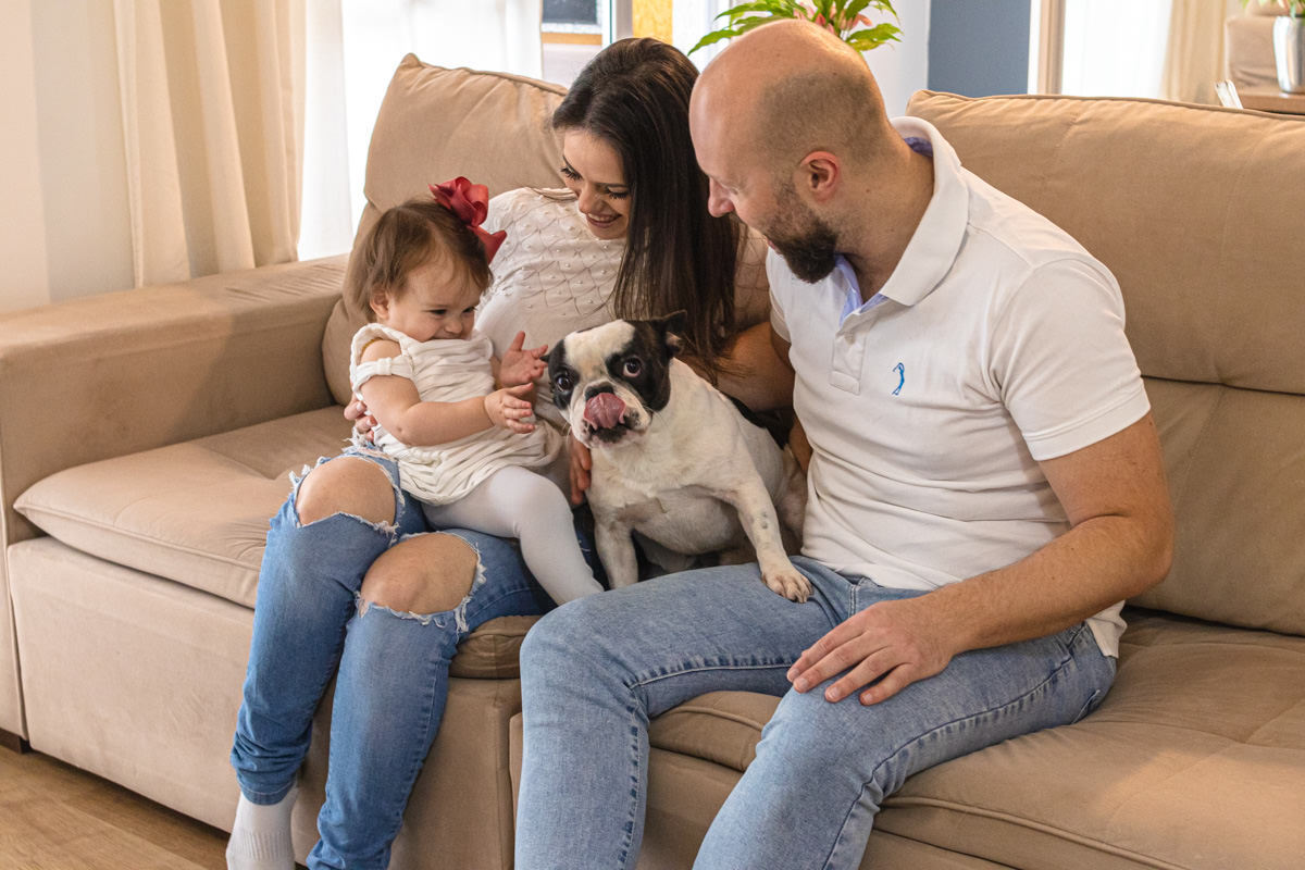 família sentada no sofá de casa com cachorro no colo 