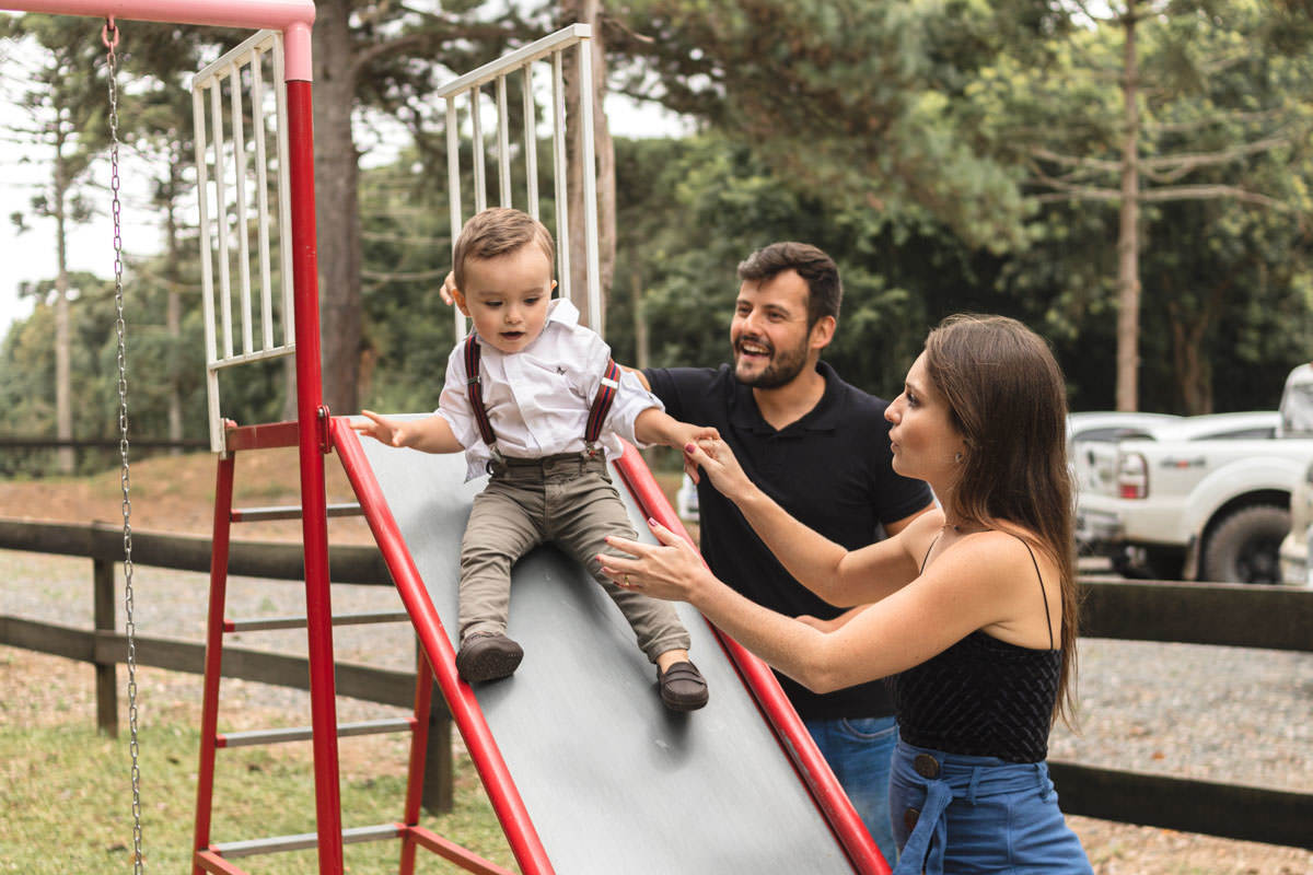 pai, mãe e filho brincando no escorrega no parque 