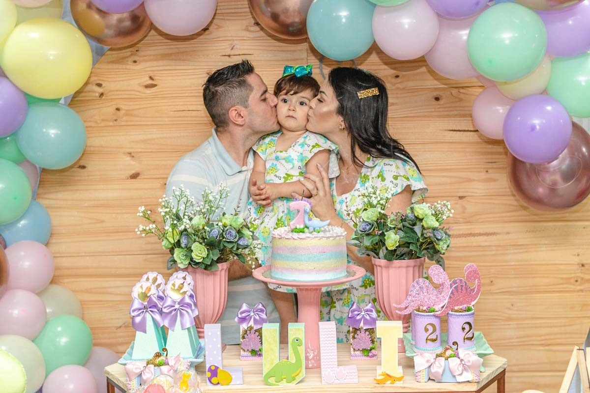pai e mãe beijando a filha na mesa do bolo de aniversário