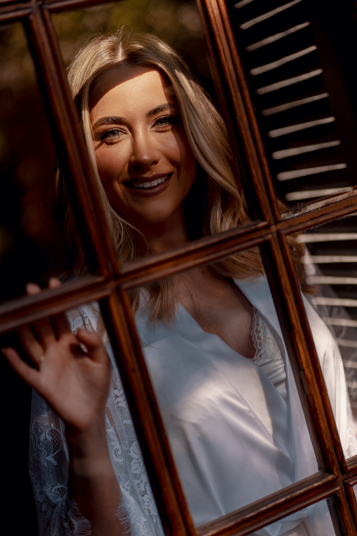 Noiva sorrindo enquanto é fotografada através da janela.