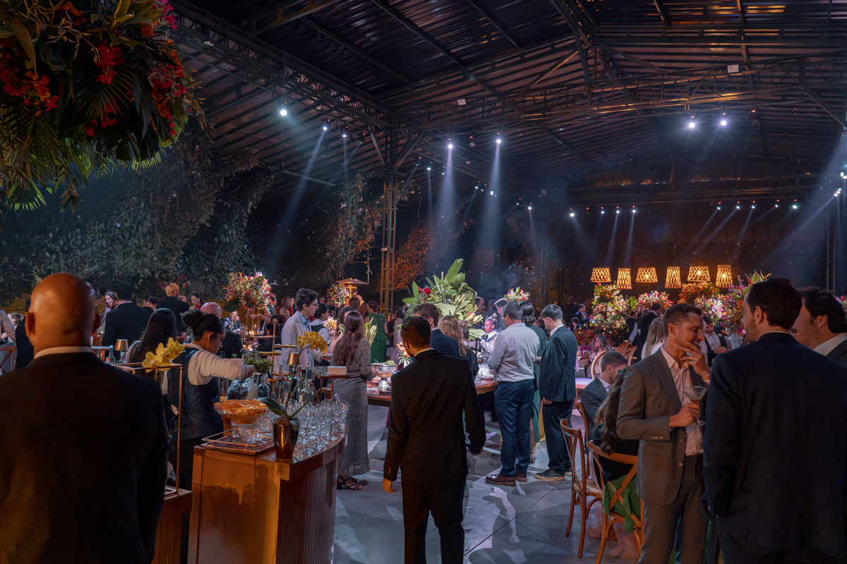 Festa de casamento à noite, com convidados reunidos sob a iluminação do espaço.