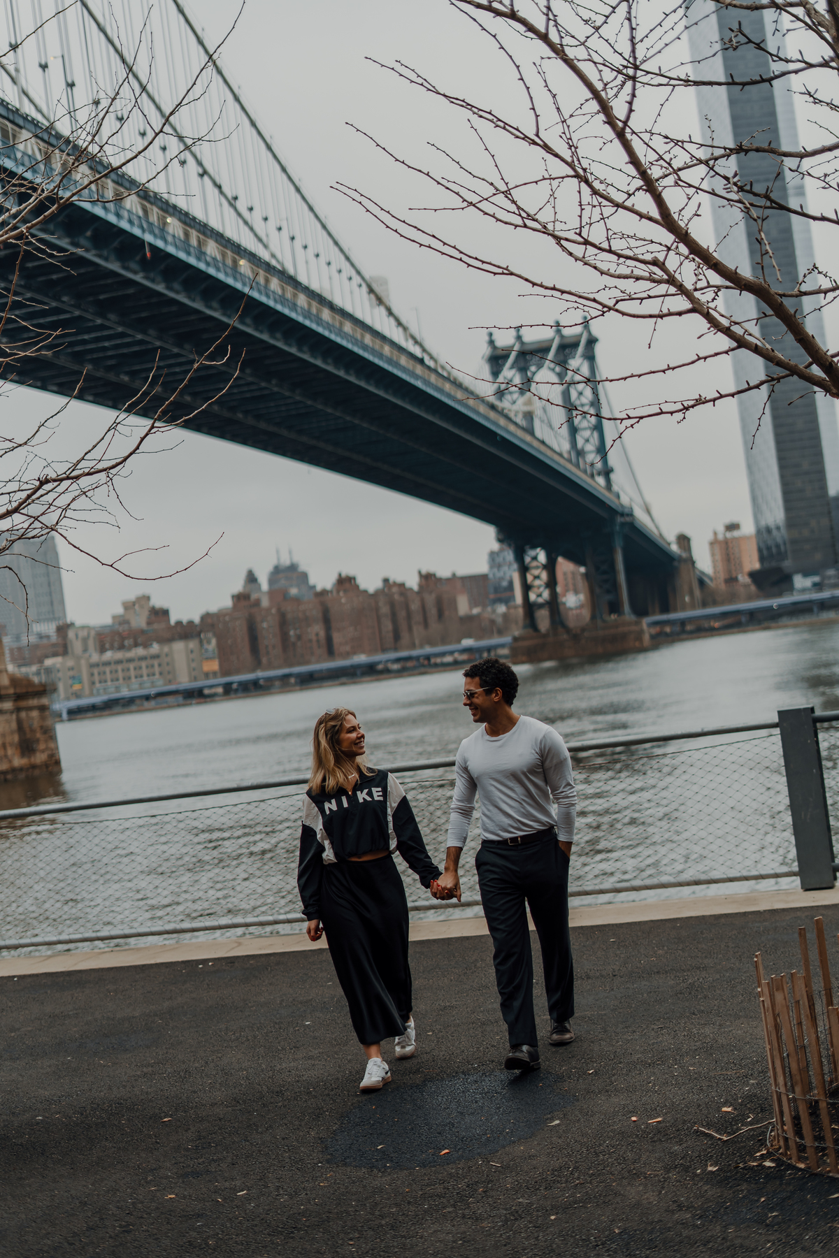 Maria Vitória e Davi junto ao rio com a Brooklyn Bridge ao fundo em Nova York.