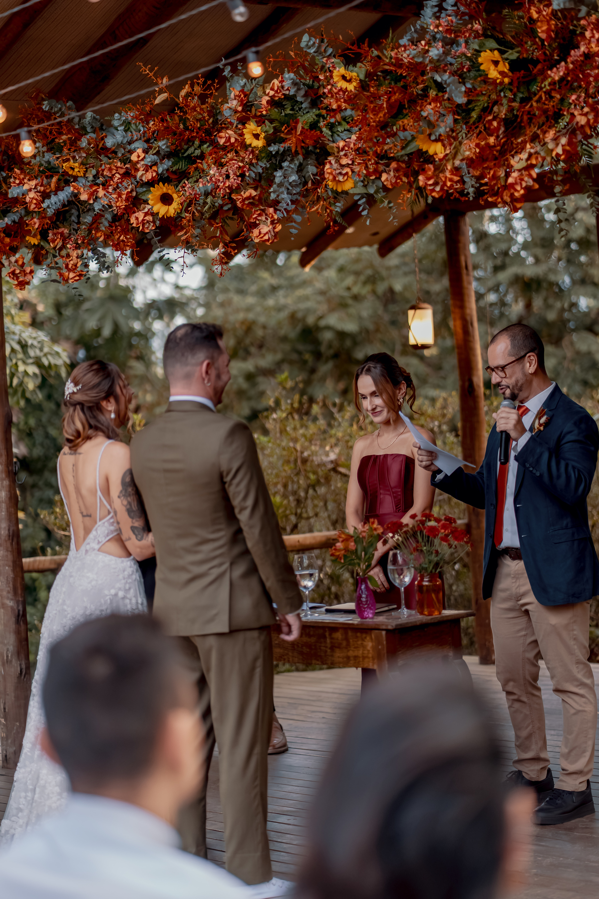 Fábio e Yasmin diante do celebrante durante um dos momentos da cerimônia, cercados pela decoração floral e pelos convidados.