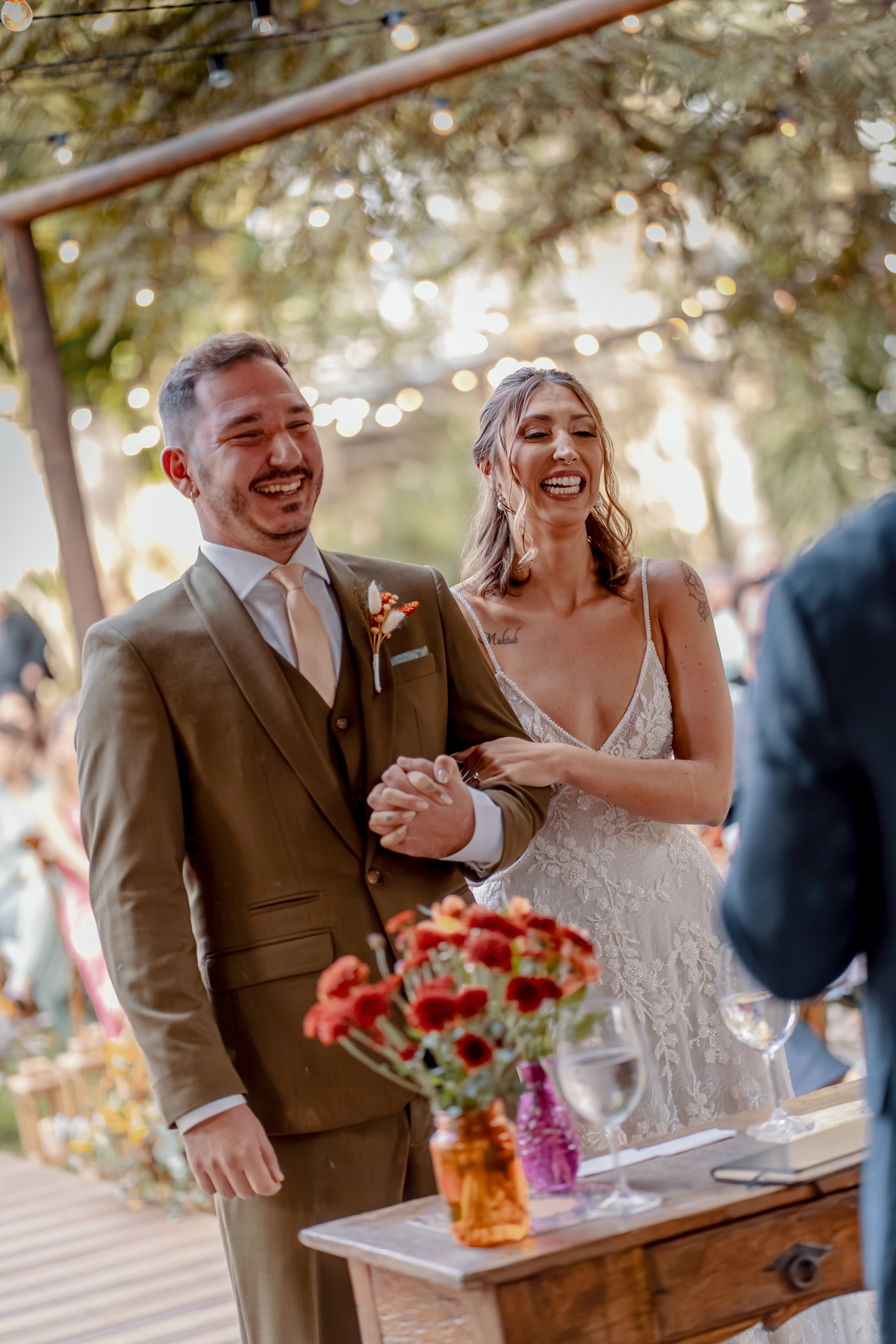 Fábio e Yasmin juntos durante a celebração, registrados com a luz natural do ambiente e a presença dos convidados ao redor.
