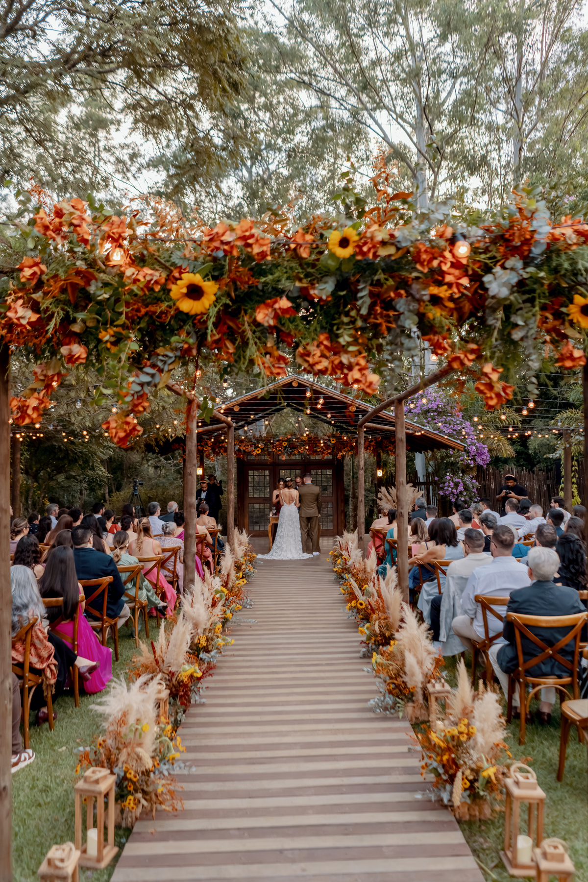 Decoração do altar da Fazenda Vila dos Eucaliptos, com flores em tons quentes criando um cenário marcante para a cerimônia no campo.
