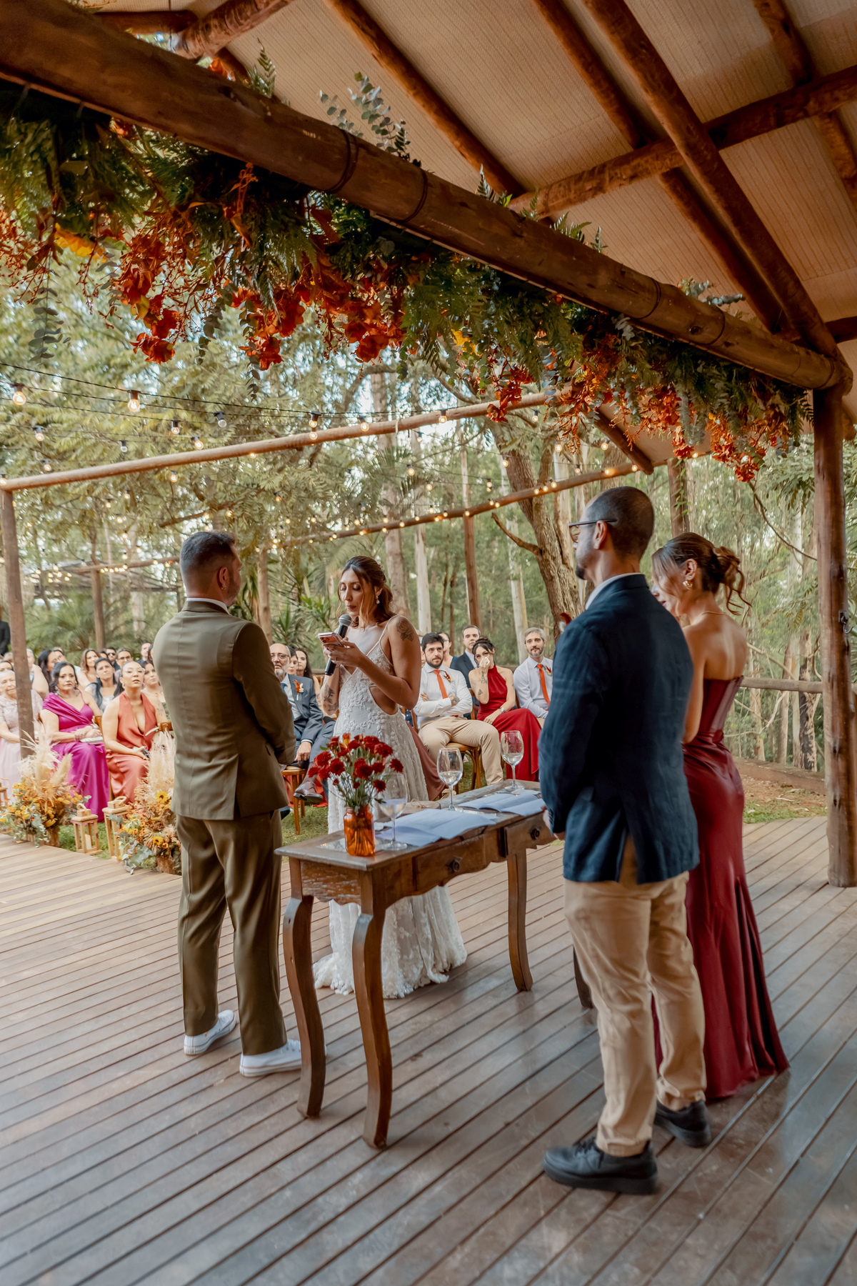 Fábio e Yasmin diante do altar durante a cerimônia ao ar livre, cercados pelos familiares e amigos que acompanharam o casamento.