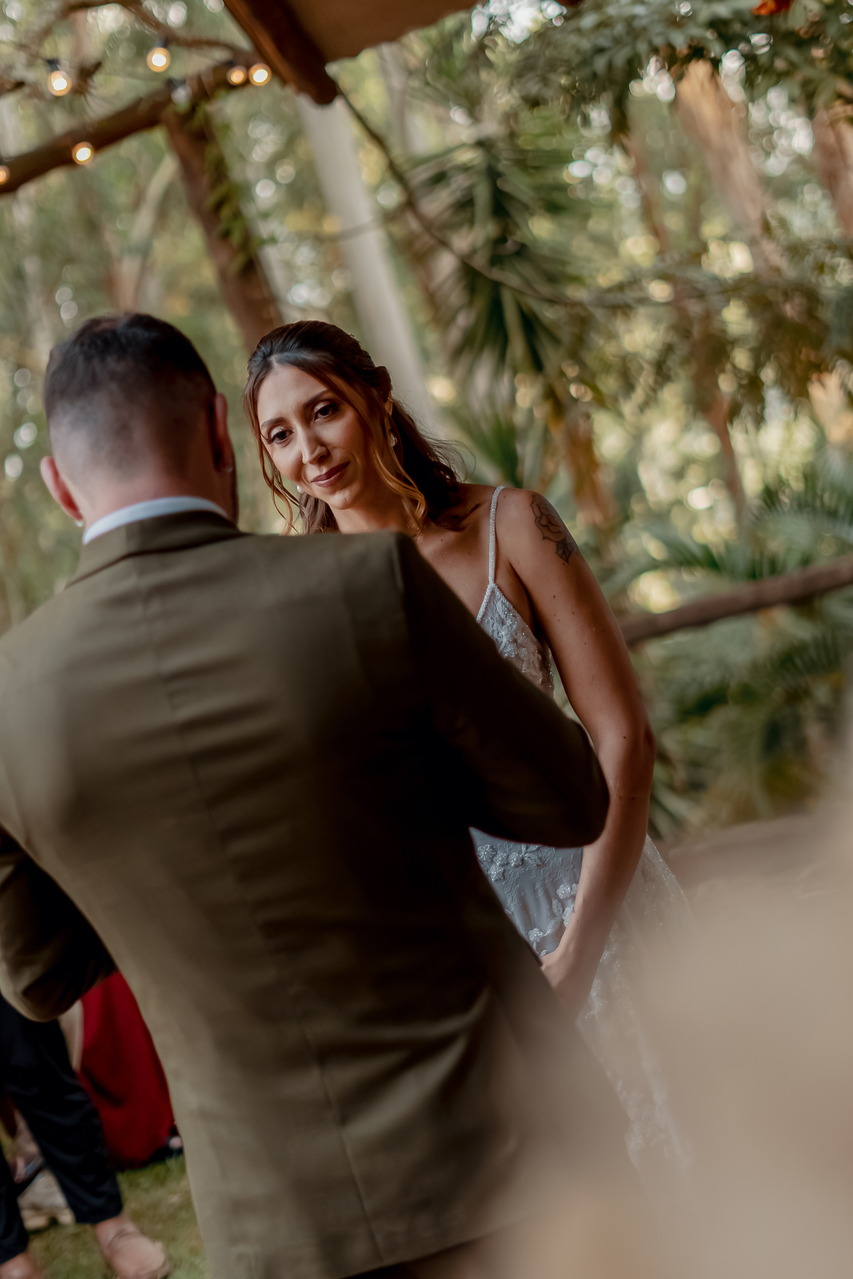 Yasmin olhando para Fábio durante a cerimônia de casamento, em um momento íntimo registrado entre os convidados e a natureza.