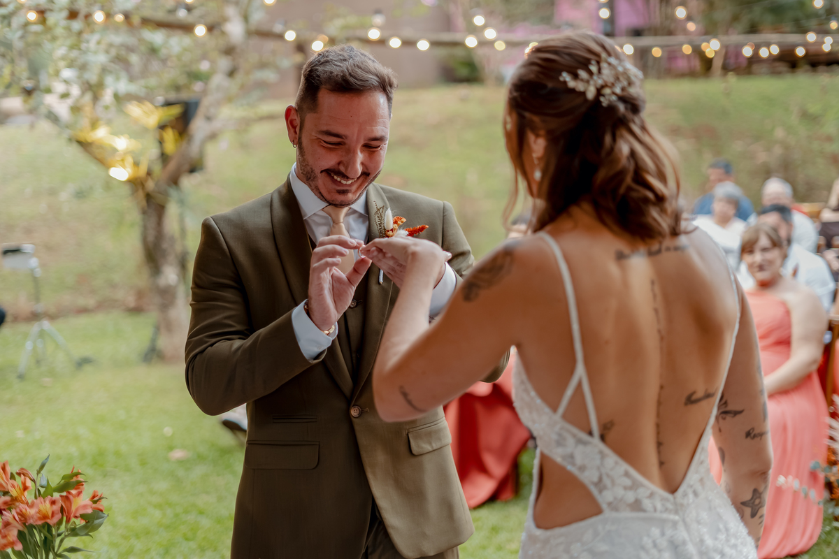 Fábio colocando a aliança em Yasmin durante a cerimônia de casamento, um dos momentos simbólicos da celebração ao ar livre.
