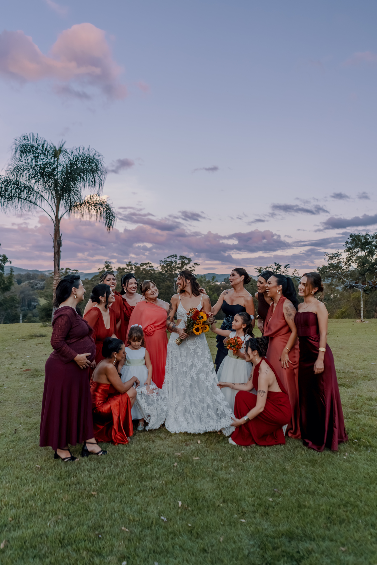 Yasmin cercada pelas madrinhas após a cerimônia, em um registro descontraído realizado ao ar livre durante o casamento no campo.