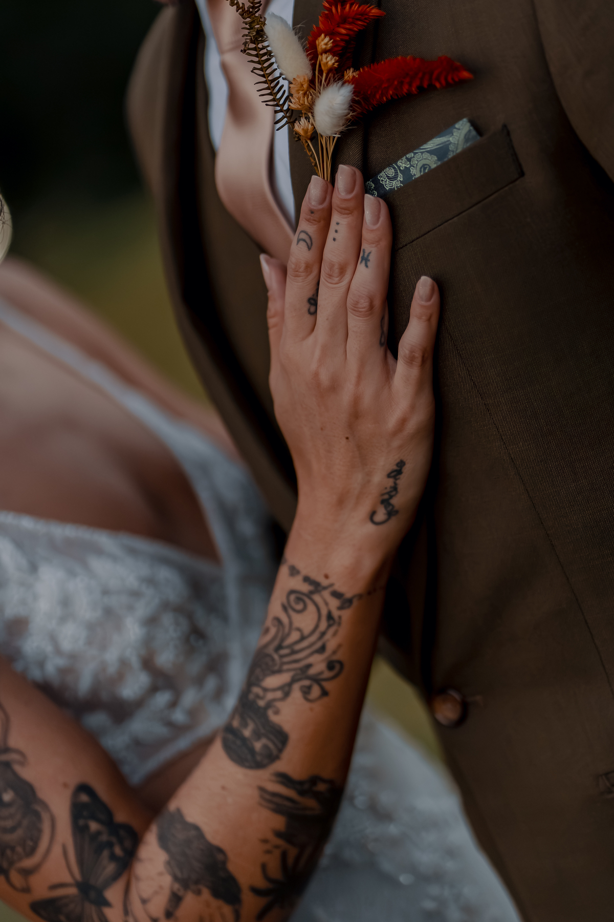 Detalhe da mão de Yasmin sobre Fábio, destacando a aliança e a tatuagem em uma fotografia intimista do casal.