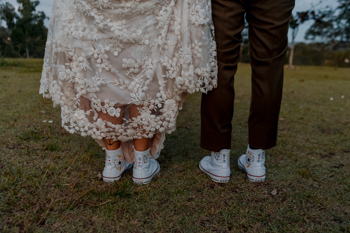 Detalhe do vestido de Yasmin e dos pés dos noivos durante o ensaio no gramado, registrando elementos do visual do casamento.