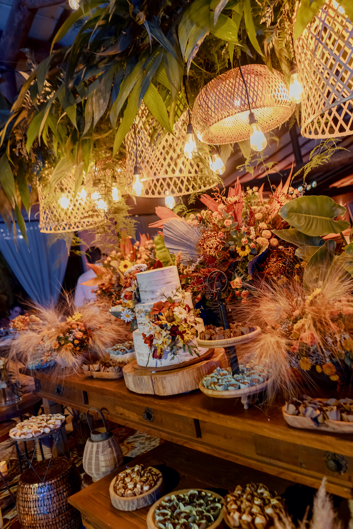 Arranjo floral da festa de Fábio e Yasmin, com flores, folhagens e iluminação quente compondo a decoração da recepção.