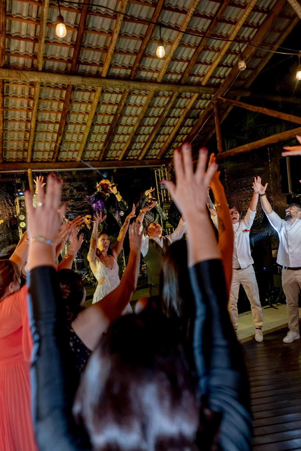 Convidados comemorando na pista de dança durante a festa, em meio à iluminação e à decoração da recepção.
