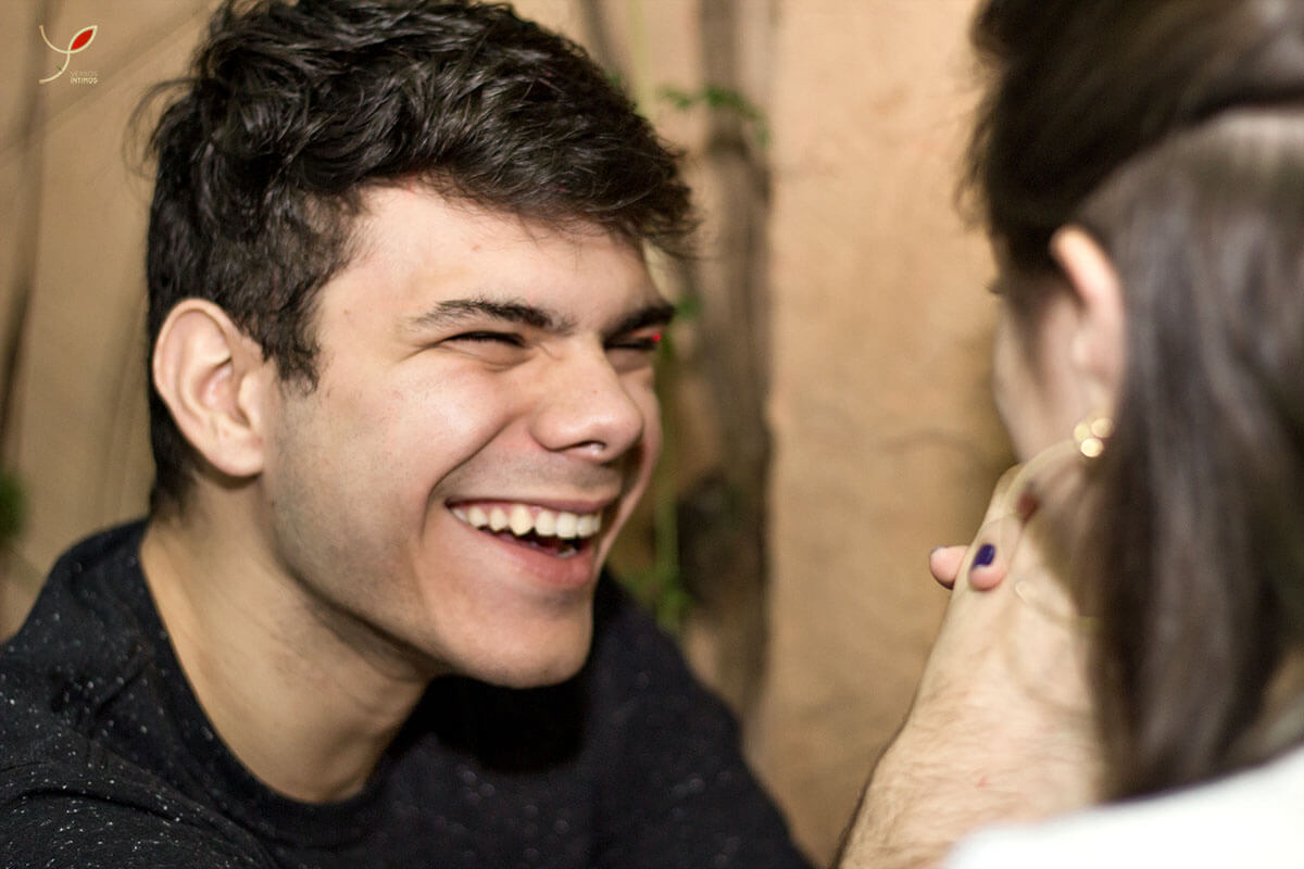 Casal sentado um na frente do outro, fazendo carinho um ao outro e sorrindo. Numa cafeteria de São José dos Campos.