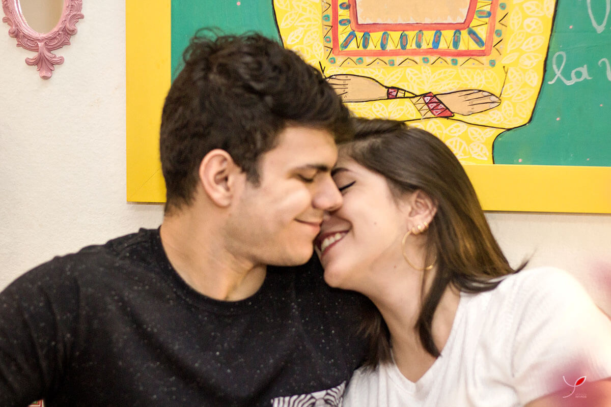 Casal sentado um na frente do outro, fazendo carinho um ao outro e sorrindo. Numa cafeteria de São José dos Campos.
