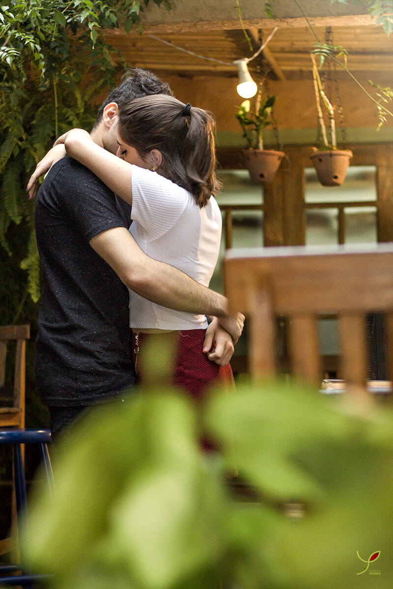 Casal sentado um na frente do outro, fazendo carinho um ao outro e sorrindo. Numa cafeteria de São José dos Campos.