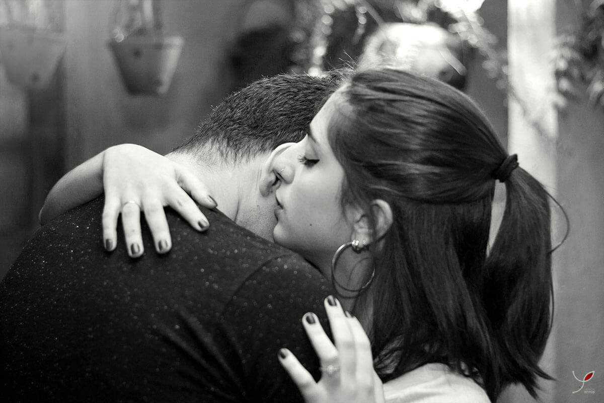 Casal sentado um na frente do outro, fazendo carinho um ao outro e sorrindo. Numa cafeteria de São José dos Campos.