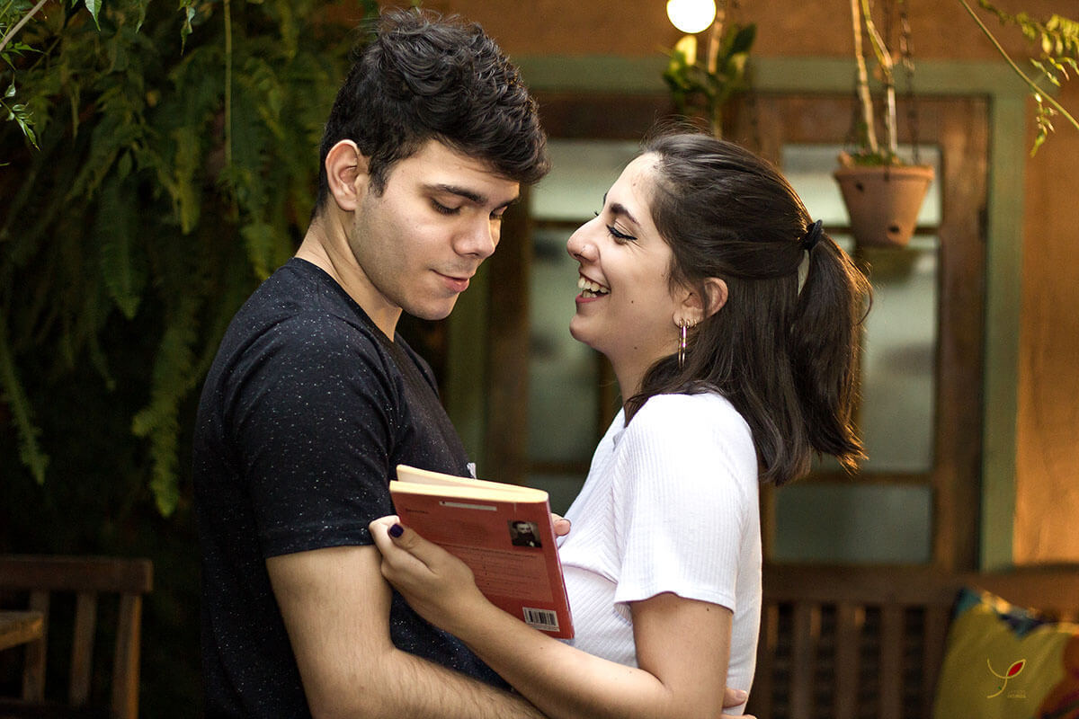 Casal sentado um na frente do outro, fazendo carinho um ao outro e sorrindo. Numa cafeteria de São José dos Campos.