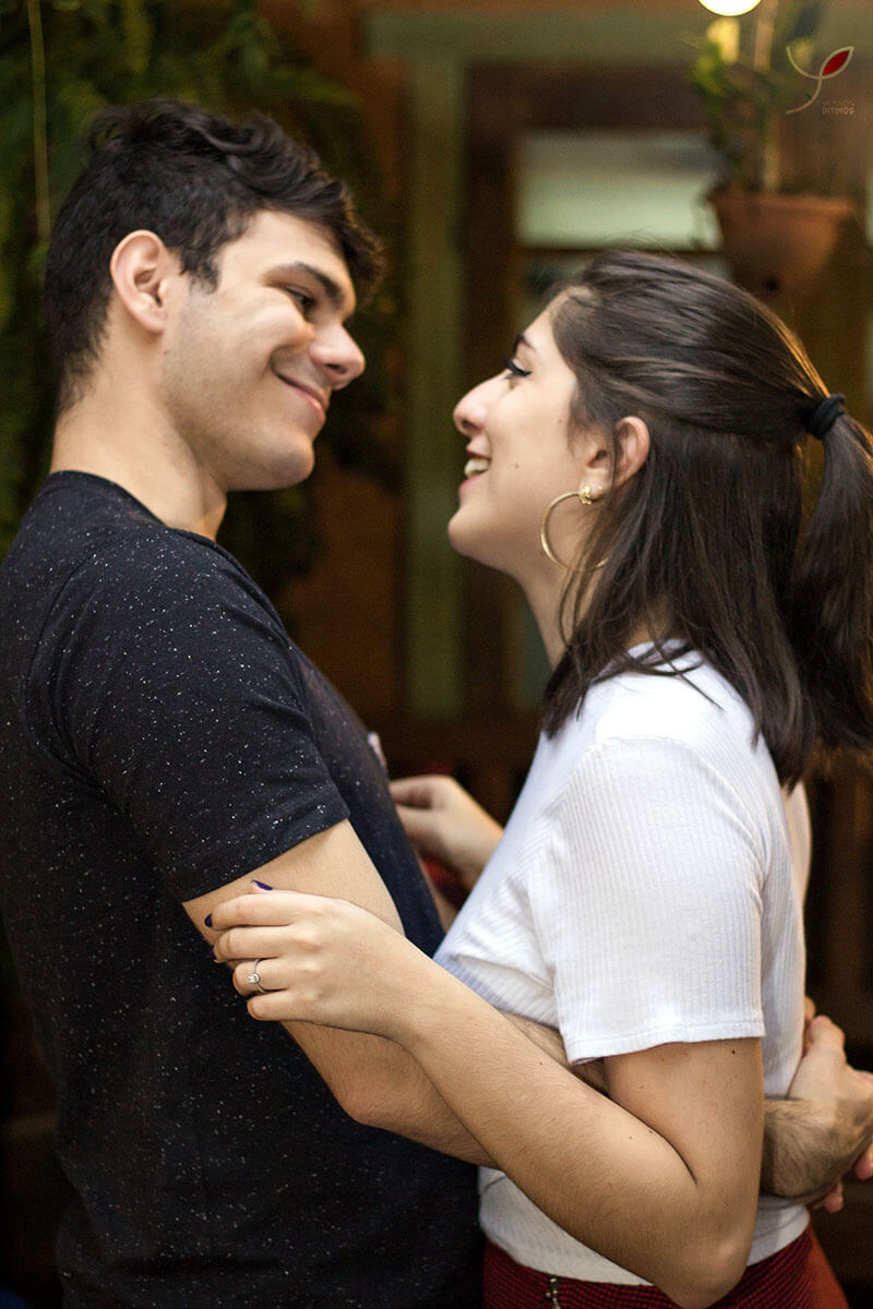 Casal sentado um na frente do outro, fazendo carinho um ao outro e sorrindo. Numa cafeteria de São José dos Campos.