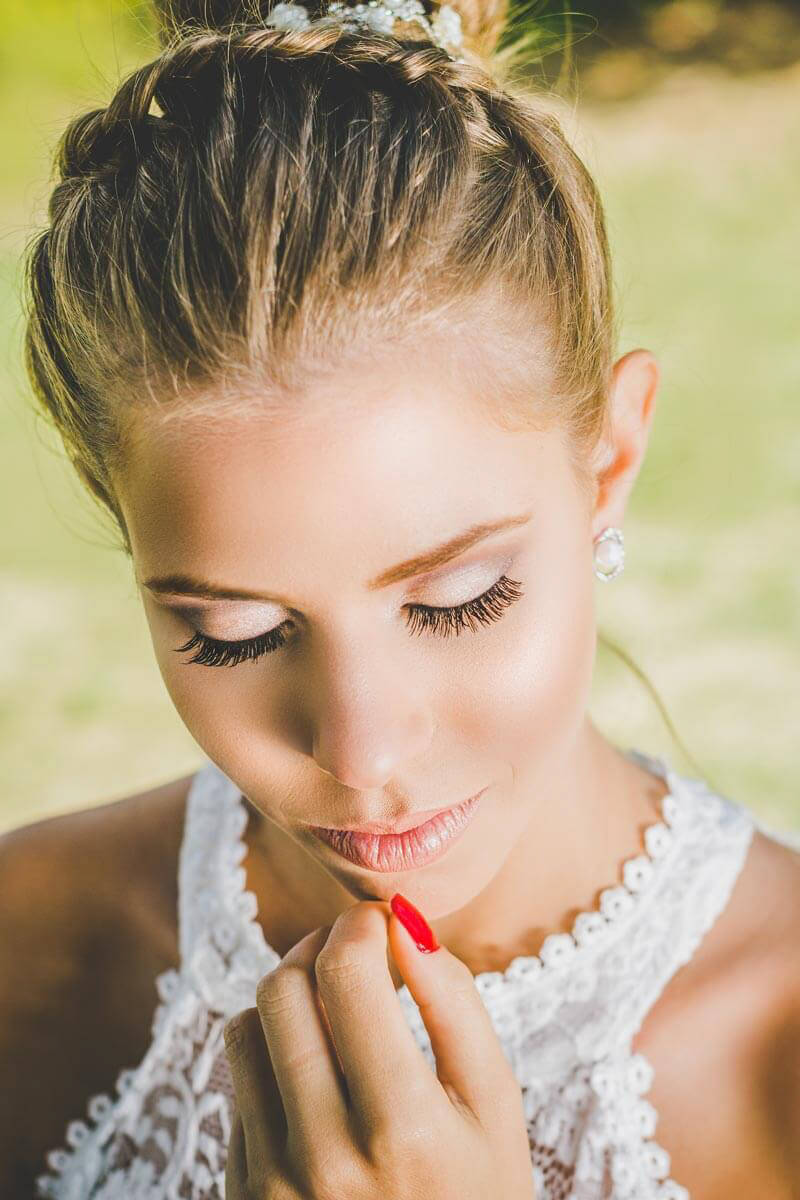 Noiva maquiada para casamento ao ar livre ou para igreja de dia. Com cabelo preso tipo coque e usando joias