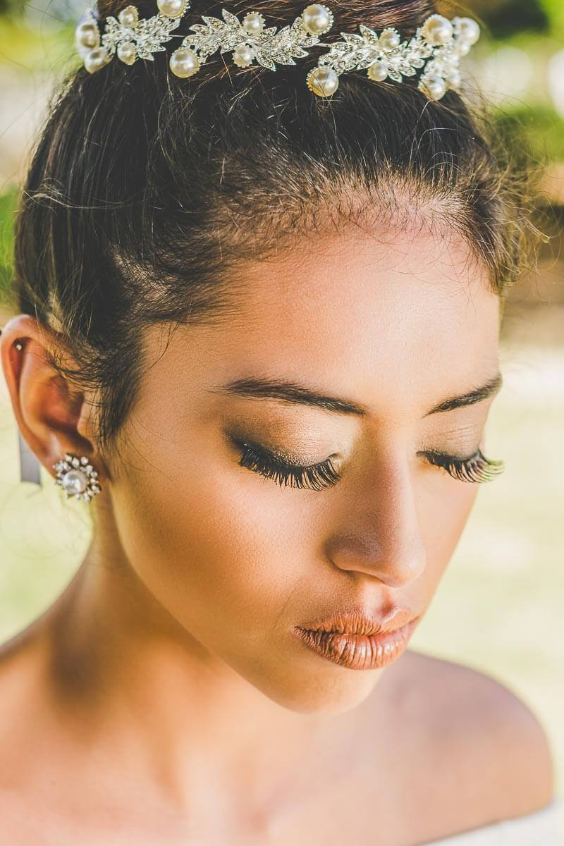 Noiva maquiada para casamento ao ar livre ou para igreja de dia. Com cabelo preso tipo coque e usando joias