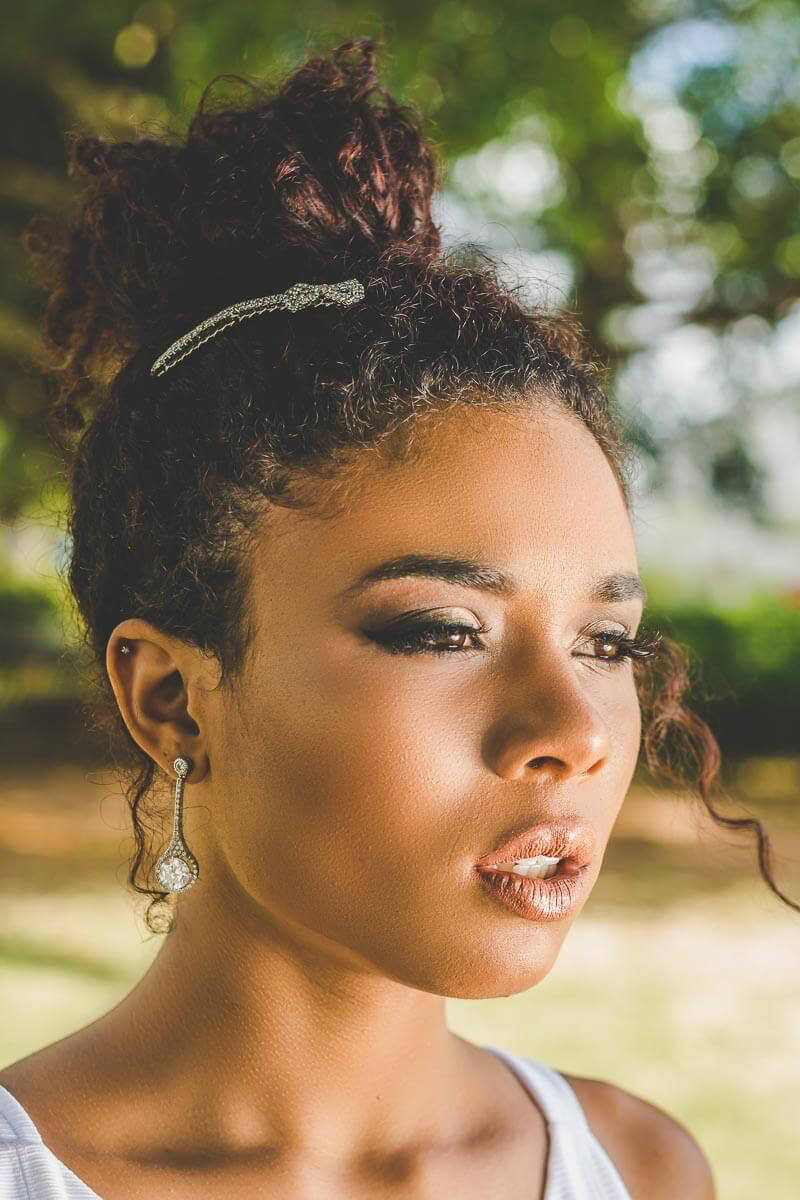 Noiva maquiada para casamento ao ar livre ou para igreja de dia. Com cabelo preso tipo coque e usando joias