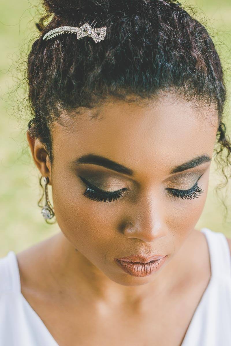 Noiva maquiada para casamento ao ar livre ou para igreja de dia. Com cabelo preso tipo coque e usando joias