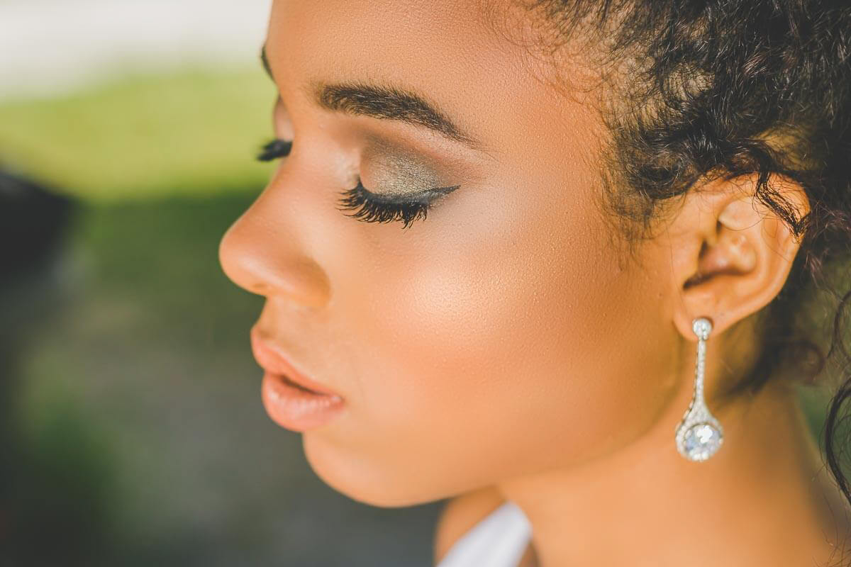 Noiva maquiada para casamento ao ar livre ou para igreja de dia. Com cabelo preso tipo coque e usando joias
