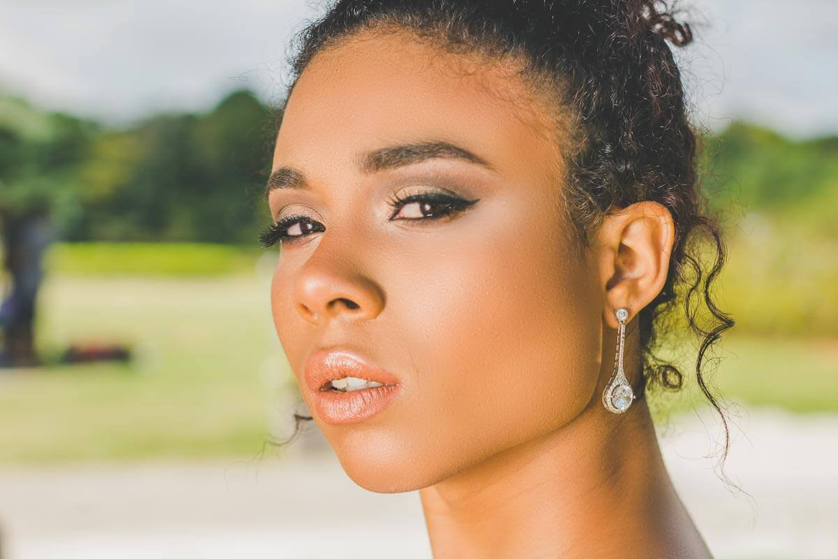 Noiva maquiada para casamento ao ar livre ou para igreja de dia. Com cabelo preso tipo coque e usando joias