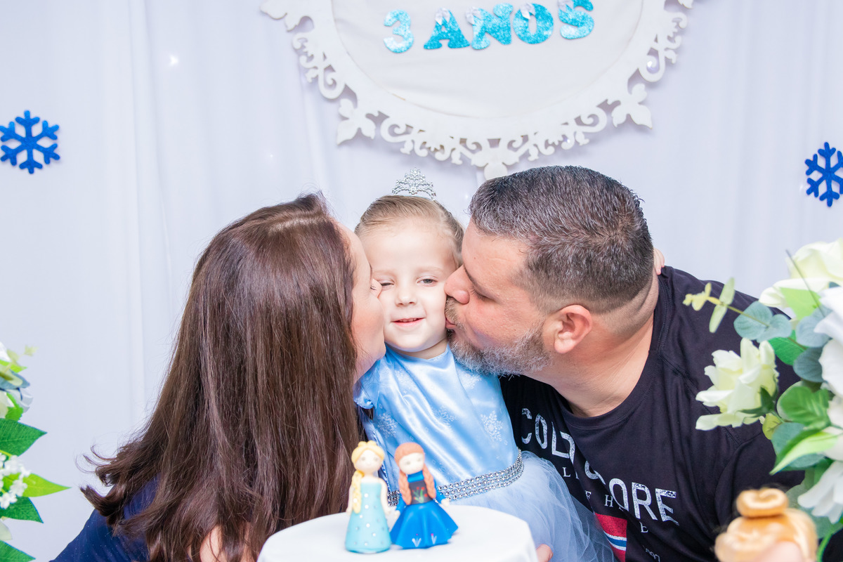 Pais beijando a aniversariante na mesa do bolo
