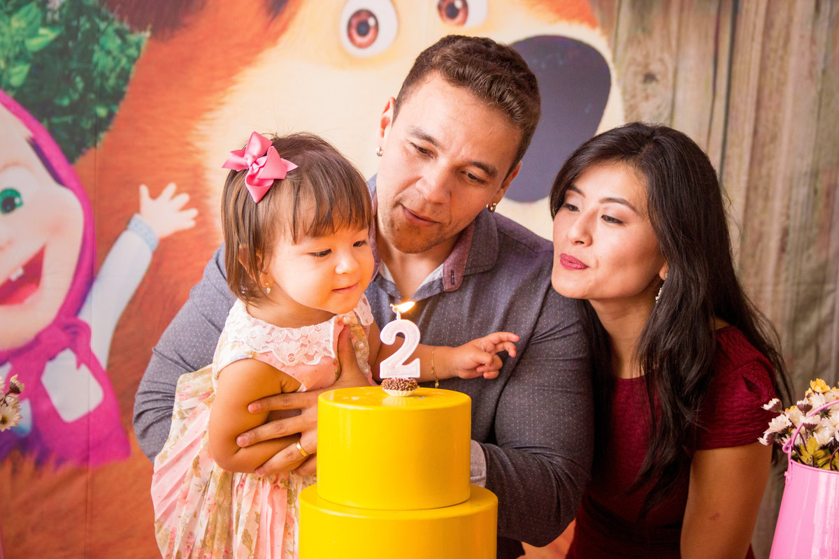 Aniversariante e seus pais assoprando as velinhas