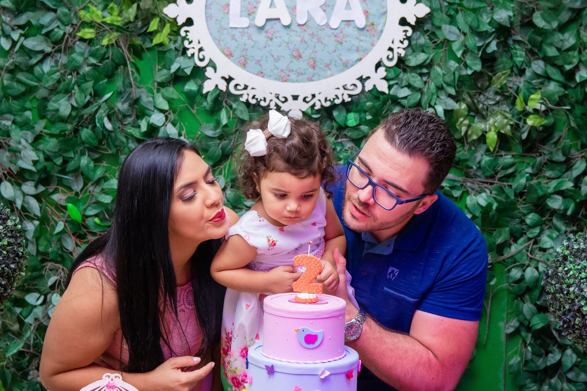 Aniversariante e seus pais assoprando as velinhas